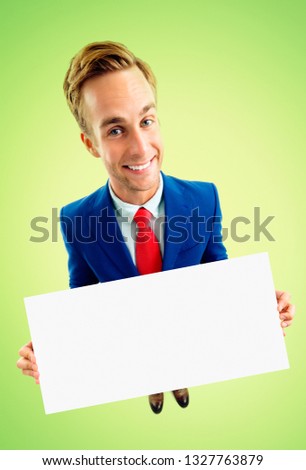Funny businessman in blue suit and red tie, showing blank signboard with copyspace area for advertising text or slogan, top angle view shot, over green background. Business concept.