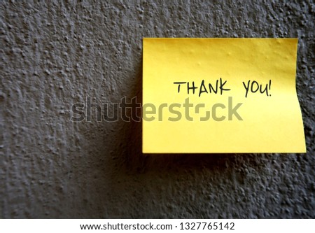 A yellow note pad stick on the grey rough textured cement wall, with a simple handwriting message THANK YOU