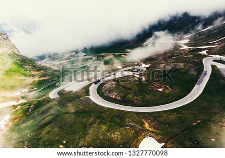 Bird's eye view of serpentine curves. Aerial view of scenic route in Austria with name Grossglockner High Alpine Road. Some of hairpin turns of Hochtor Pass. cloudy sky and snowy mountains Royalty-Free Stock Photo #1327770098