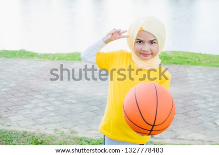 Kid female in hijab play basketball in park