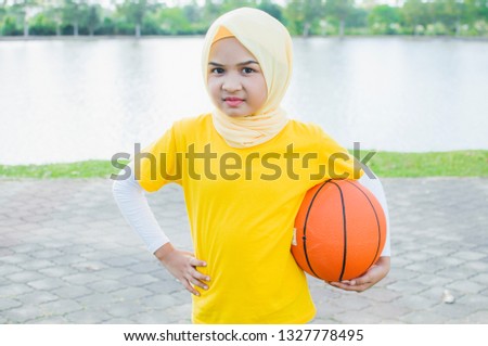 Kid female in hijab play basketball in park