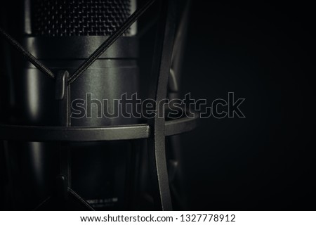 Abstract close up of a studio microphone to the left of the frame against a dark background, horizontal aspect. Focus on front cord.