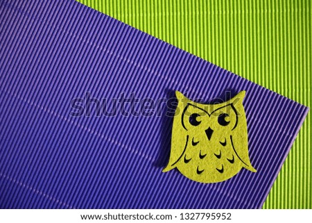 Decorative figurine of a green felt owl on a background of corrugated cardboard of violet color 
