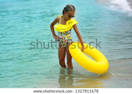 Portrait of happy modern child in yellow swimwear with yellow inflatable lifebuoy on the seashore