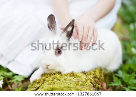 Beautiful  little girl in a white dress plaing with white rabbit in the spring wood. Close up picture. Easter time
