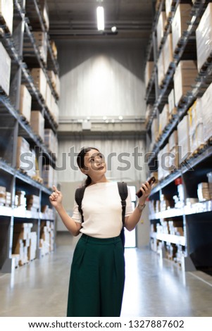Woman shopping for furniture in warehouse and use smart phone for check price
