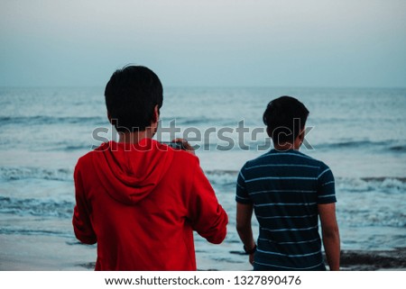 Boy taking photograph of his friend through mobile phone while standing at Nagoa beach in Diu, India