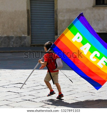Unidentified child with rainbow flag with "peace" (Latin and Italian: Pace) written on it, in a  bad abondoned neighbourhood. Concept of world peace and no war movements Royalty-Free Stock Photo #1327891103