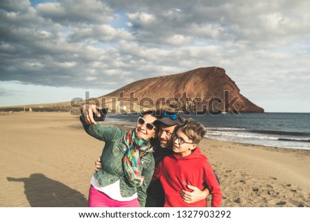 Dad mom with son taking selfie smiling and happy at the beach near the ocean. Parents with child on holiday making pictures for memories of an exotic vacation. Family portrait mountain sea cloudy sky 