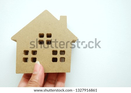 Woman hand holding a mini wooden house on white background.
