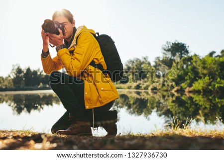 Photographer taking photos of nature sitting beside a lake on a sunny day. Traveler capturing the beauty of nature in camera in a countryside location.