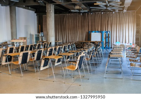 lateral view of a training room/conference hall interior with rows of wood chairs with a small table for each of them