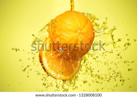 Orange splashing juice, water, on a yellow background.