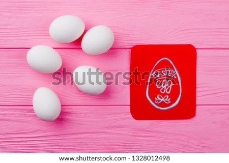 Easter eggs and red greeting card. White chicken eggs and picture of egg on red paper card. Kids congratulation with Easter.