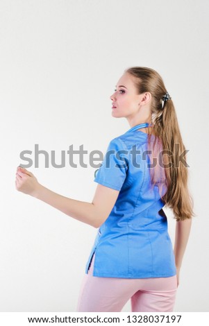 Woman doctor blond young bright gray background studio day beautiful one looks with a smile joy invites gesture to follow. Hospitality friendly care support.