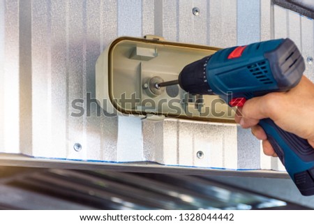Man hand using impact cordless drill driver to drive the screw while installing the lamp.