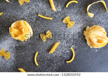 Different types of pasta such as tagliatelle, penne and farfalle lie on a dark marble surface - concept with different uncooked noodles on a dark background