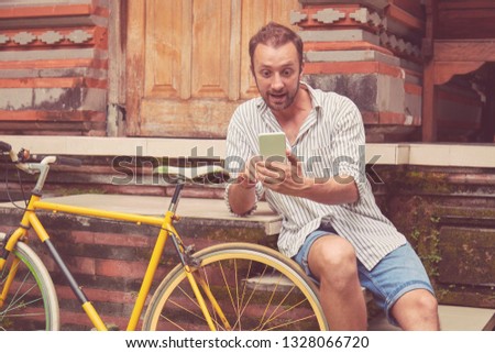 Modern man using cellphone while sitting with old bicycle.