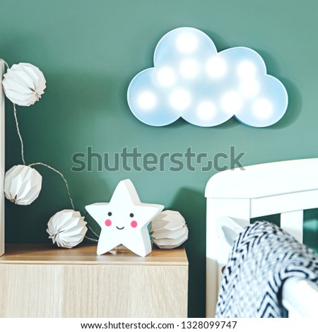 The modern and cute scandinavian newborn baby room with blue cloud, cotton lamps, star and baby cot. Sunny and bright interior. Green background walls.