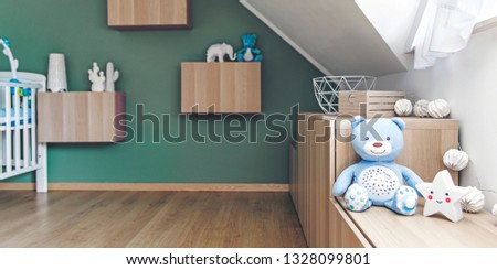 Stylish and cute scandinavian newborn baby room with hanging wooden shelfs, baby cot, toys, star lamp and teddy bears. Modern green background wall. Bright and sunny interior. 