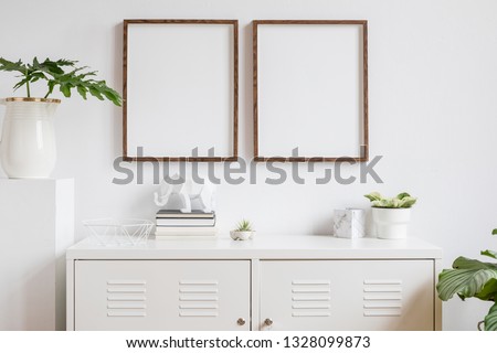 Stylish scandi home interior with two brown wooden mock up photo frames with books, beautiful plants in vase, elephant figure and home accessories. Minimalistic concept of white room decor.