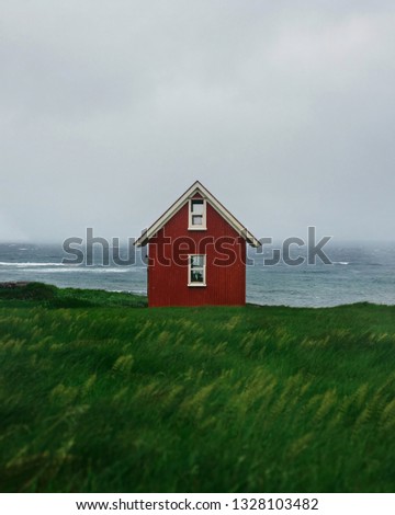 Old red wooden house on cliff with grey ocean on background.