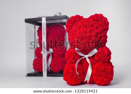 Red  teddy bear of foamirane roses. The same teddy in clear box with black paper cover on background. White stripe on teddy neck. Stock photo isolated on white background.
