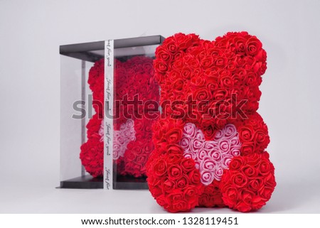 Red  teddy bear toy of foamirane roses. The same teddy in clear box with black paper cover on background. Pink heart in teddy paws. Stock photo isolated on white background.