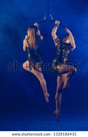 Duet gymnasts girls aerial acrobatics on the ring on the background of blue smoke