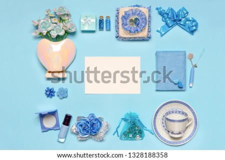 Stylish feminine accessories, flowers, cosmetics, gifts and decorative items in blue pastel colors on blue background. Empty white card for text, mock up. Women's or mother's day concept. Flat lay