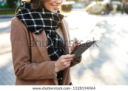 Cropped picture of a beautiful happy young woman outdoors walking by street using tablet computer.