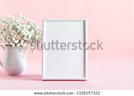 Home interior floral decor. White gypsophila flowers, photo frame. Elegant floral soft pink composition. Beautiful flowers in vase on pastel pink wall background