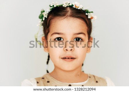 Close up image little girl adorable hairstyle with flowers, smiling brightfully, looking to the camera with happy expression. Toddler beautiful girl posing on light grey studio wall. People, emotion