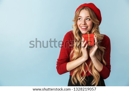 Image of happy blond woman 20s wearing red beret holding present box isolated over blue background in studio