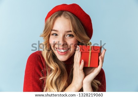 Image of attractive blond woman 20s wearing red beret holding present box isolated over blue background in studio