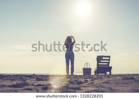 Woman standing near sun lounger and taking a picture on the mobile phone. Beach at sunset. Summer concept.