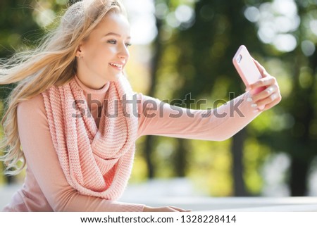Young girl making selfie and talking on cell phone. Attractive woman outdoor with mobile. Female making picture on the smartphone.