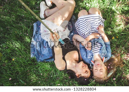 Young mother and her daughter making selfie on mobile. Girls making picture on cell phone and having fun. Pretty girlfriends. Mom and her child outdoor.