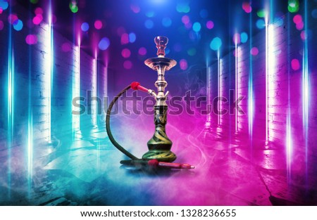 Background of smoking hookah on the background of an empty room with a concrete floor and brick walls. Neon lights, neon shapes and smoke