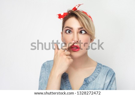 Closeup portrait of funny crazy crossed eyes young woman in casual blue denim shirt with makeup and red headband standing looking and picking her nose. indoor studio shot, isolated on white background