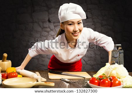 Asian woman cook leaned over the table and looking into the camera