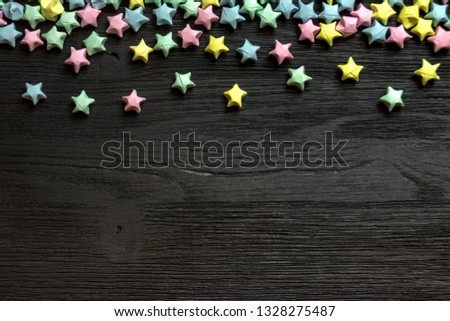 Beautiful background with light multi-colored paper stars on a black wooden surface