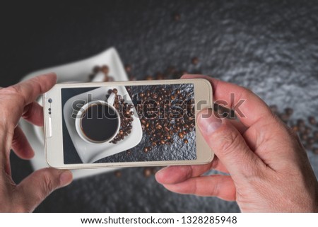 Man taking photo of White cup of coffee and coffee beans on black stone table top view