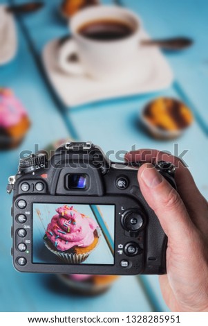 Man taking photo of Chocolate cupcake with colored pink and green cream on blue table