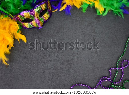 Festive New Orleans Mardi Gras Venetian Carnival Mask, Yellow, Green, Purple & Blue Feather Boa and Beads Necklace Over Chalkboard Black Background with Copy Space, Horizontal, Shot from Above