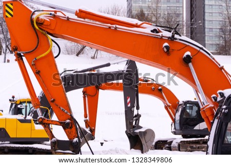 three bright tracked excavators are parked on a snowy field, booms and sticks form an enfilade