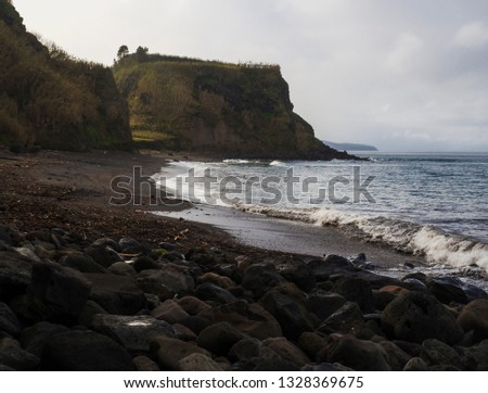 Praia da Viola beach with grassy sandstone cliffs and volacanic rock boulders, atlantic ocean landscape, Sao Miguel island Azores island Portugal