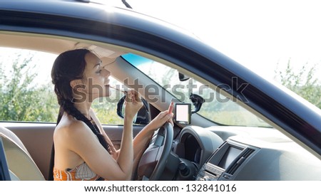 View through the side window of a female driver applying make-up using the rear view mirror in the car
