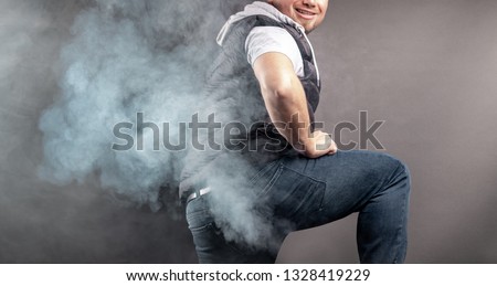 Man lift the leg and fart in front of grey background Royalty-Free Stock Photo #1328419229