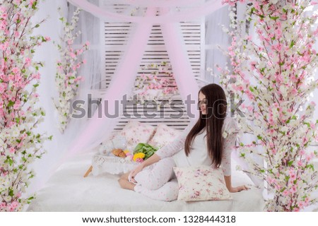 Women's day mornings.What a great morning! Attractive young woman on the bed decorated with pink and white flowers at home.Breakfast coffee in bed.women day.